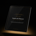A tablet displaying a black 'Torah Life Planner' cover with gold and white text, set against a dark background with a warm spotlight at the bottom.