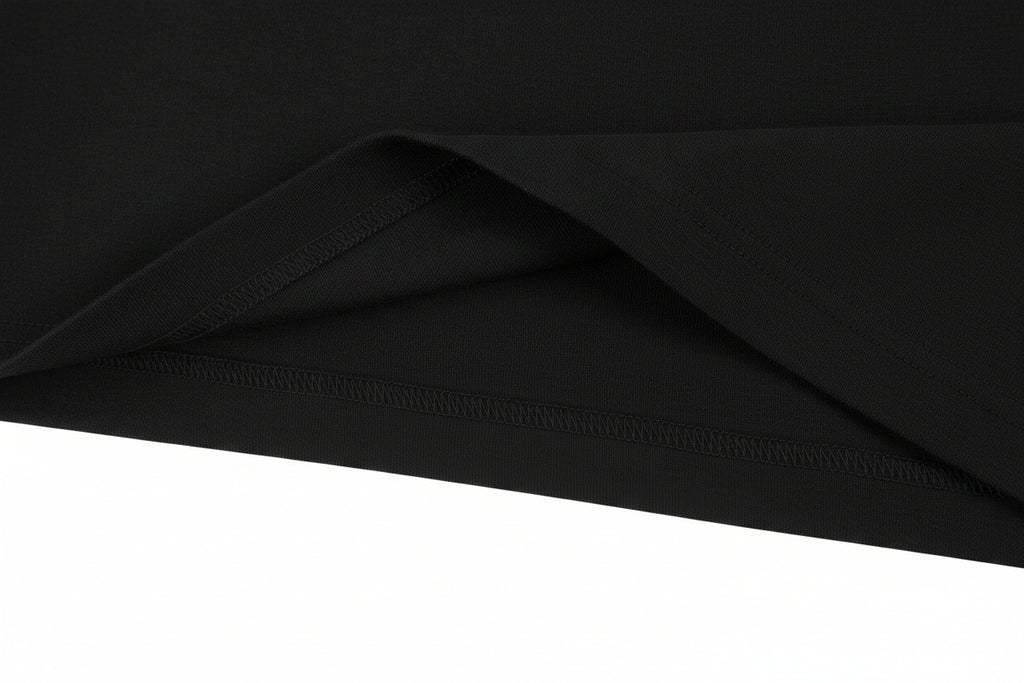 A close-up of a black fabric, likely a t-shirt, showing a folded corner to highlight the texture and hem stitching against a plain white background.