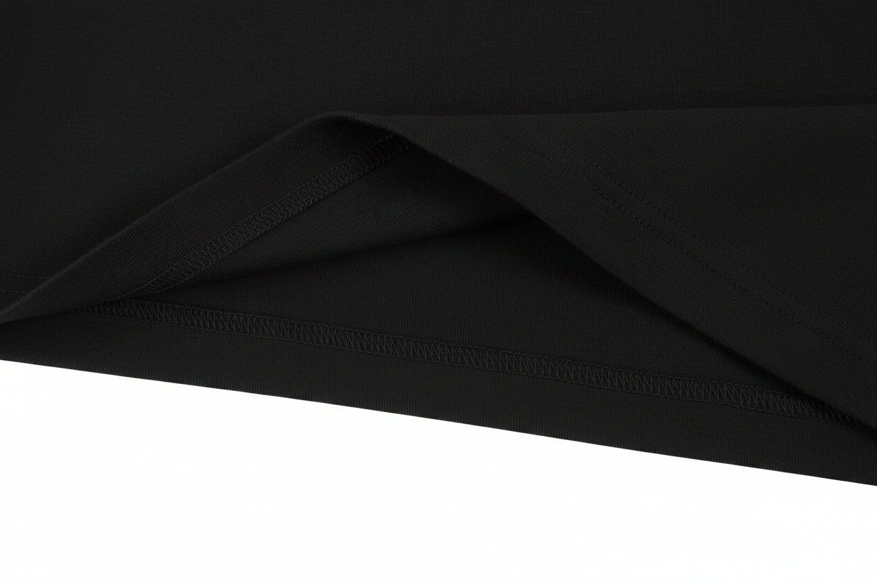 A close-up of a black fabric, likely a t-shirt, showing a folded corner to highlight the texture and hem stitching against a plain white background.