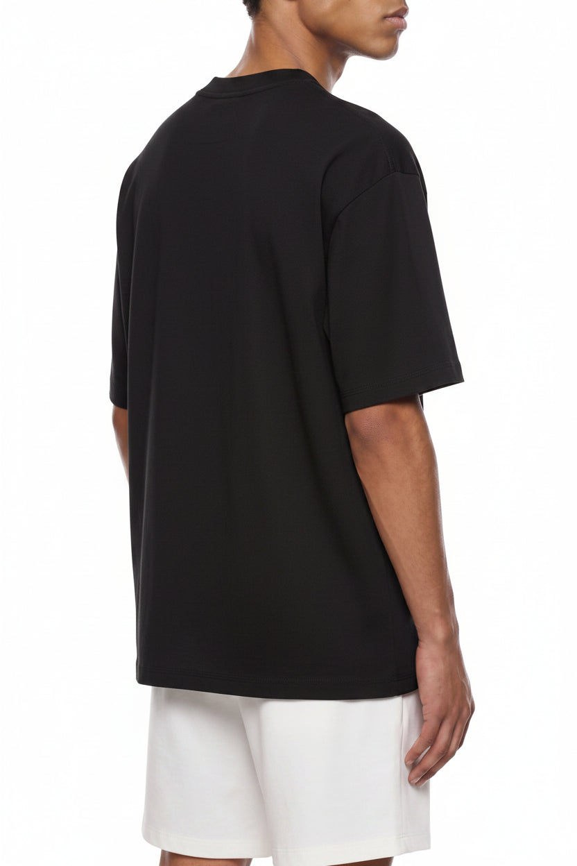A man wearing an oversized  black short-sleeve t-shirt, shown from a side-back angle against a plain white background.