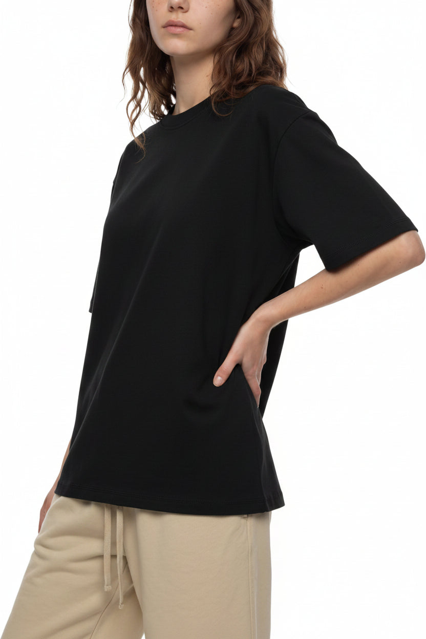 A woman wearing an oversized black short-sleeve t-shirt and beige drawstring pants, shown from the side against a plain white background.
